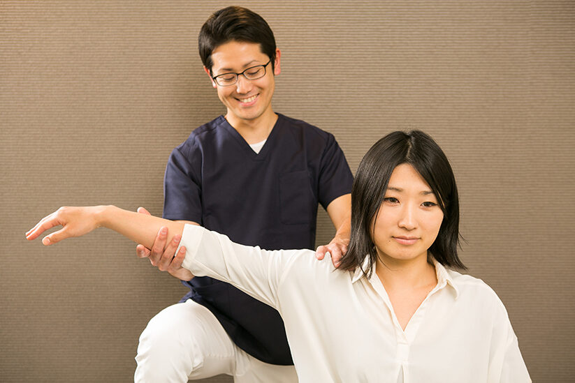 立ったまま腕を上げて肩の動く範囲を確かめる場面