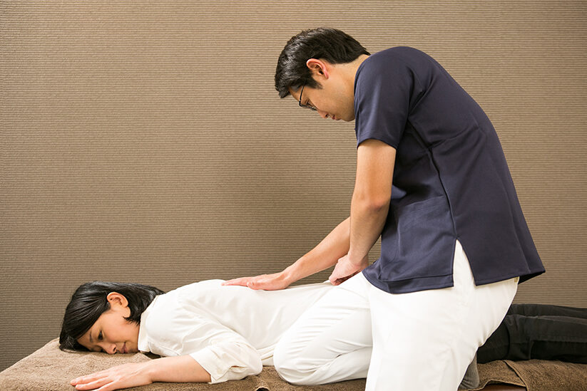 うつ伏せに寝た方の腰から骨盤にかけて、両手を当てているところ