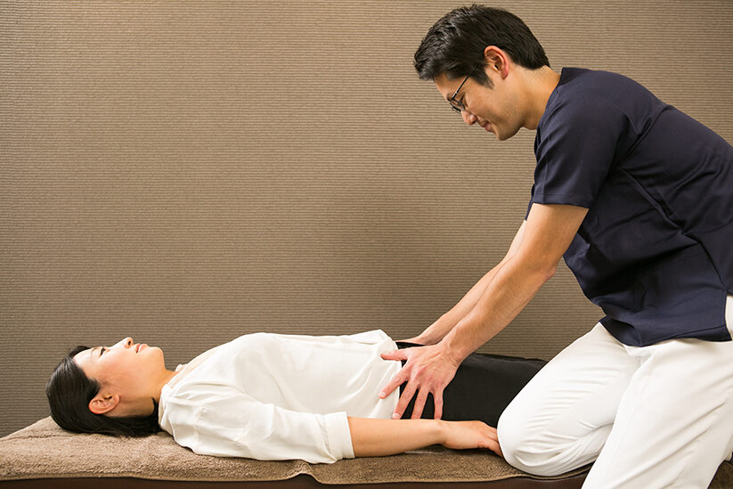 仰向けに寝た方の腰から骨盤のあたりに手を当てて、状態を確かめているところ