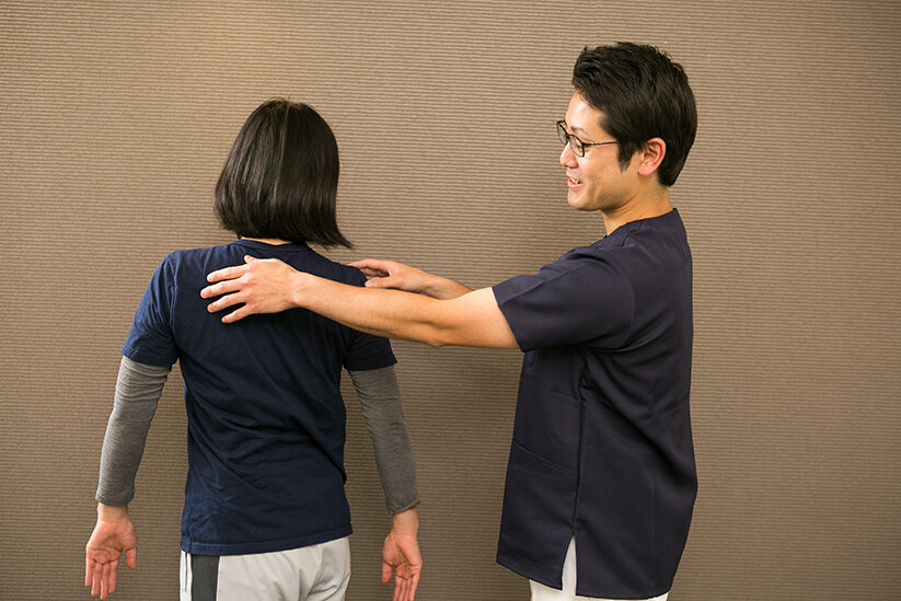 立った方の後ろから両肩に手を当てて、左右の高さを比べているところ