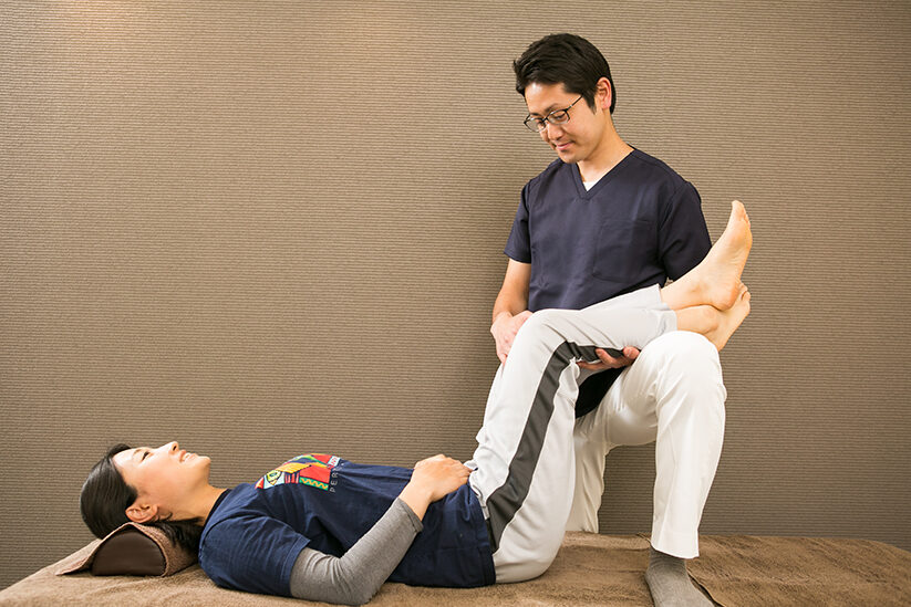 仰向けに寝た方の片脚を持ち上げ、膝を曲げて支えているところ