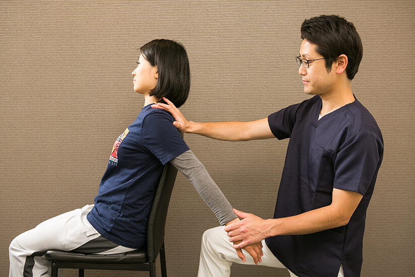 椅子に座った方の肩と前腕を持って、腕を後ろへ引いているところ